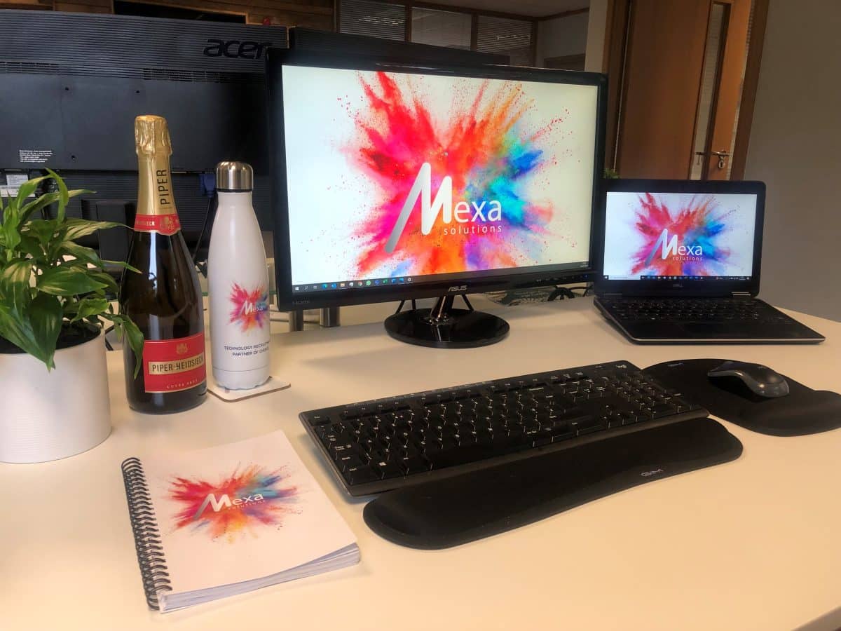 Desk showing the Laptop, Mexa Branded goodies and Champagne - welcoming you to the business on your first day.