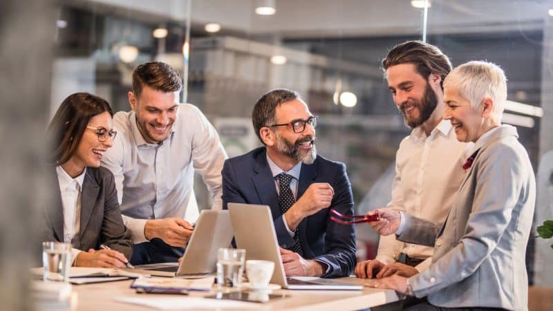 group of workers laughing and joking round a desk in an office