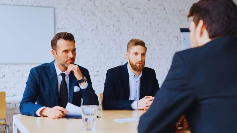 2 men sat at a table interviewing a man