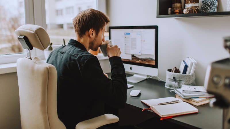 Man sat at home working from his desk drinking a coffee