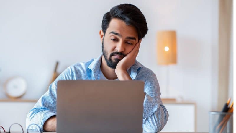 man looking bored as he stares at his laptop